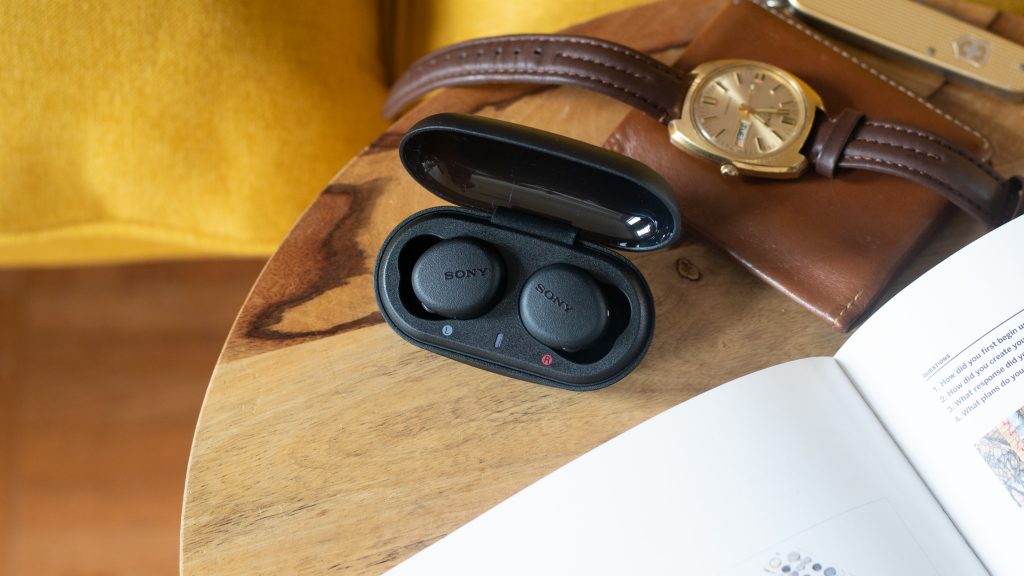 Sony WF-XB700 true wireless earbuds on wooden stool next to gold watch and swiss army knife.