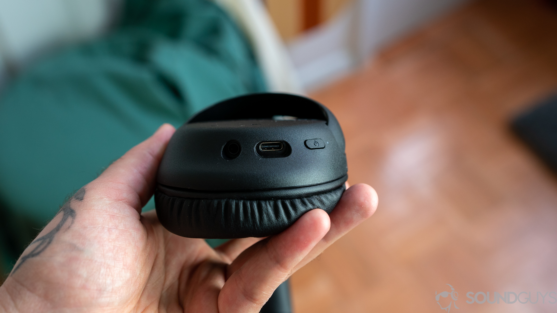 Man holding Sony WH-CH710N in hand with focus on the inputs on the left earcup with a green jack in the background