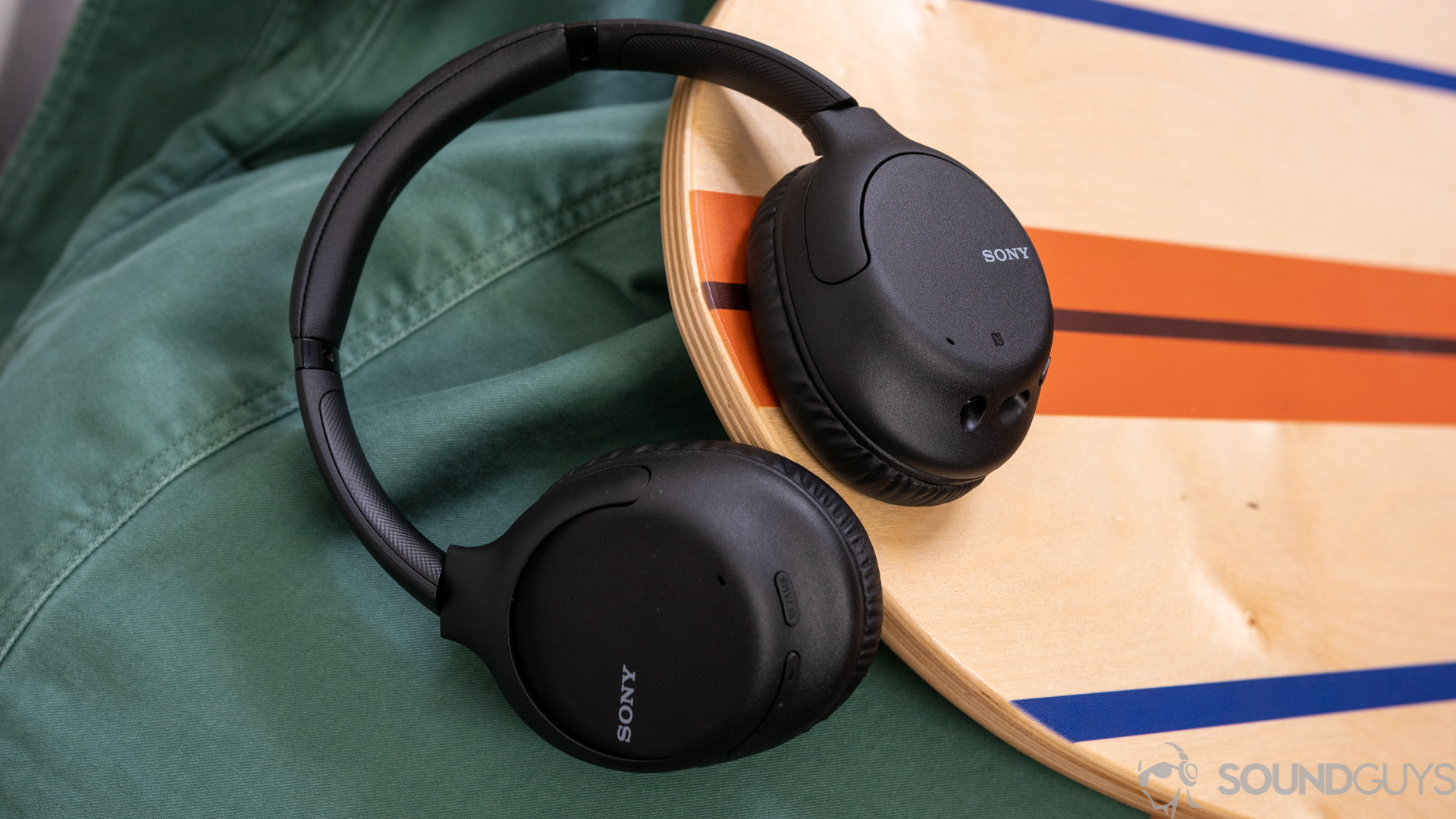 A picture of the Sony WH-CH710N noise canceling headphones on a wooden balance board and green jacket