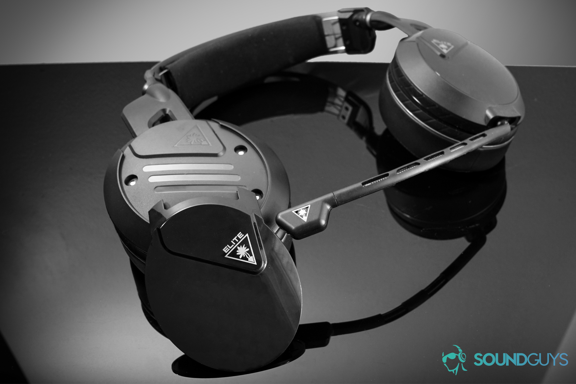 The Turtle Beach Elite Atlas gaming headset lays flat on a reflective black surface with its magnetic headphone plate detached.