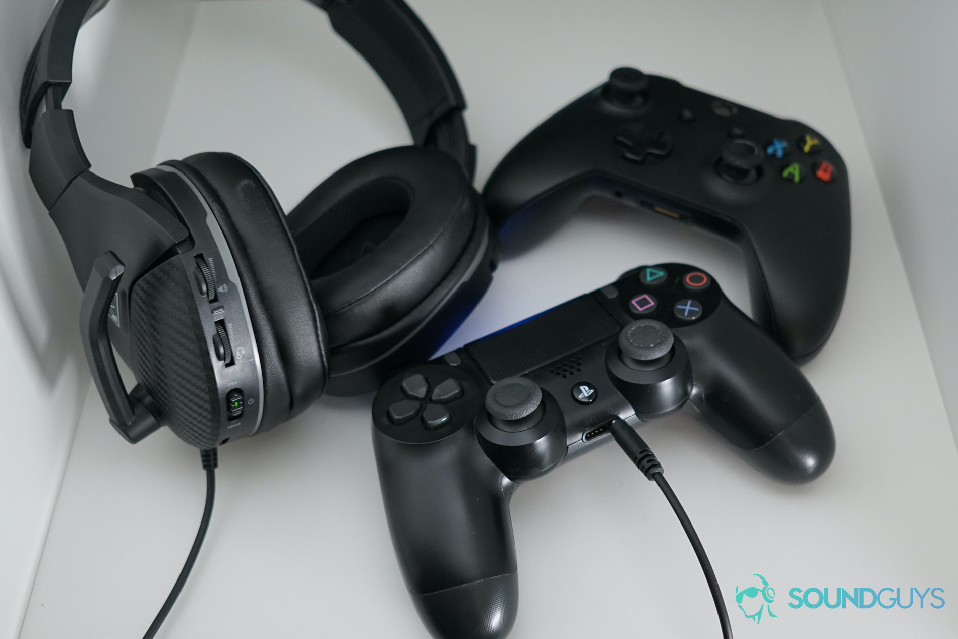 The Turtle Beach Recon 200 sits on a shelf next to a Playstation Dualshock 4 controller and an Xbox One controller