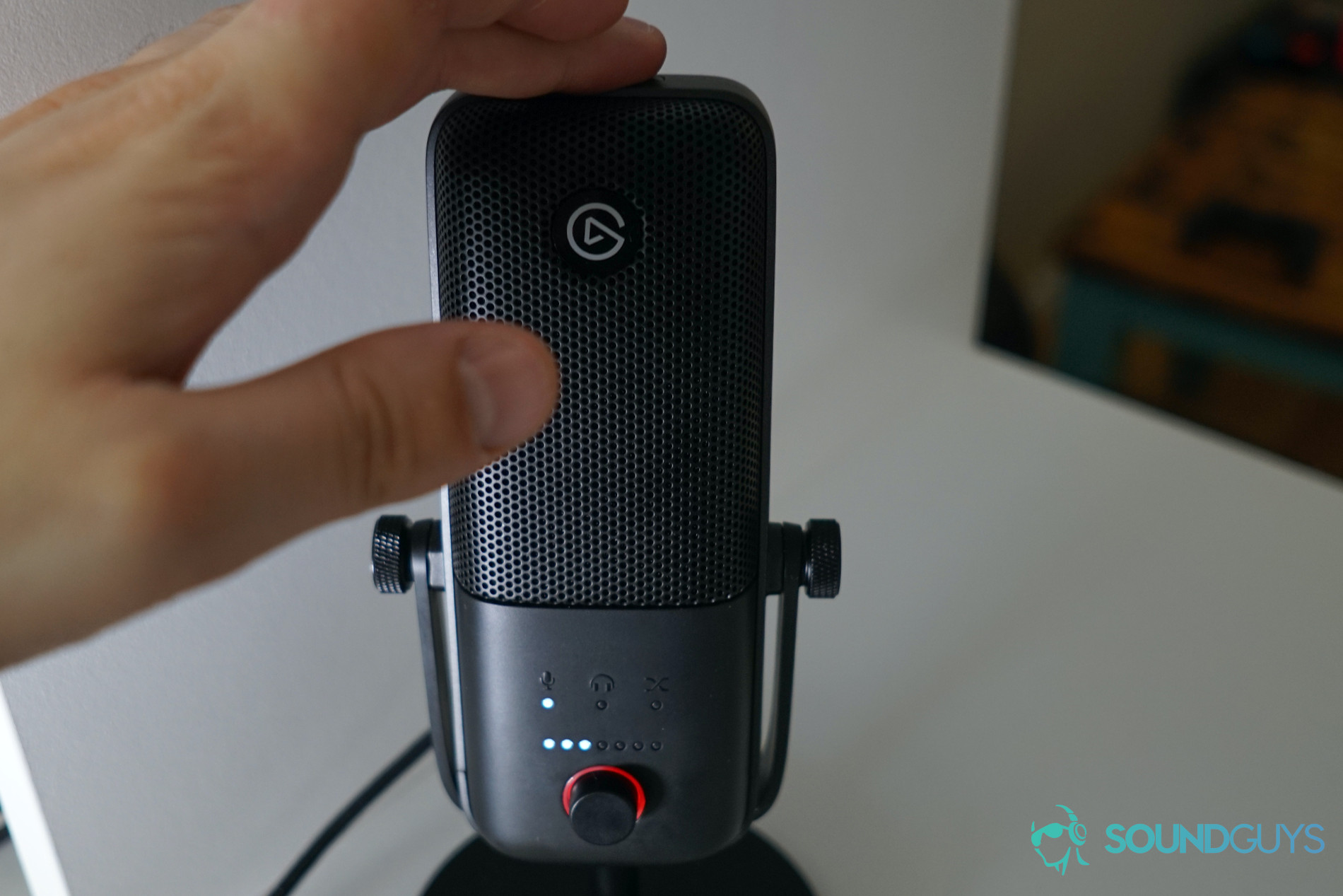 Finger pressing the mute button on top of the Elgato Wave 3 microphone
