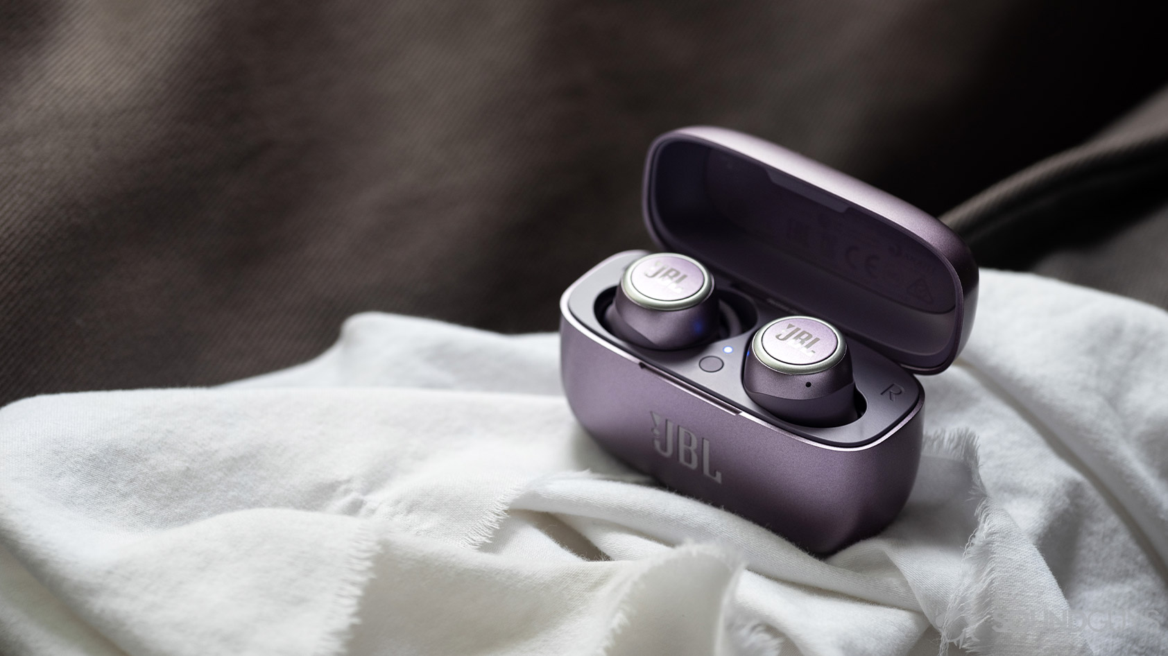 The JBL LIVE 300 TWS true wireless earbuds in the open charging case on top of a white cloth surface.