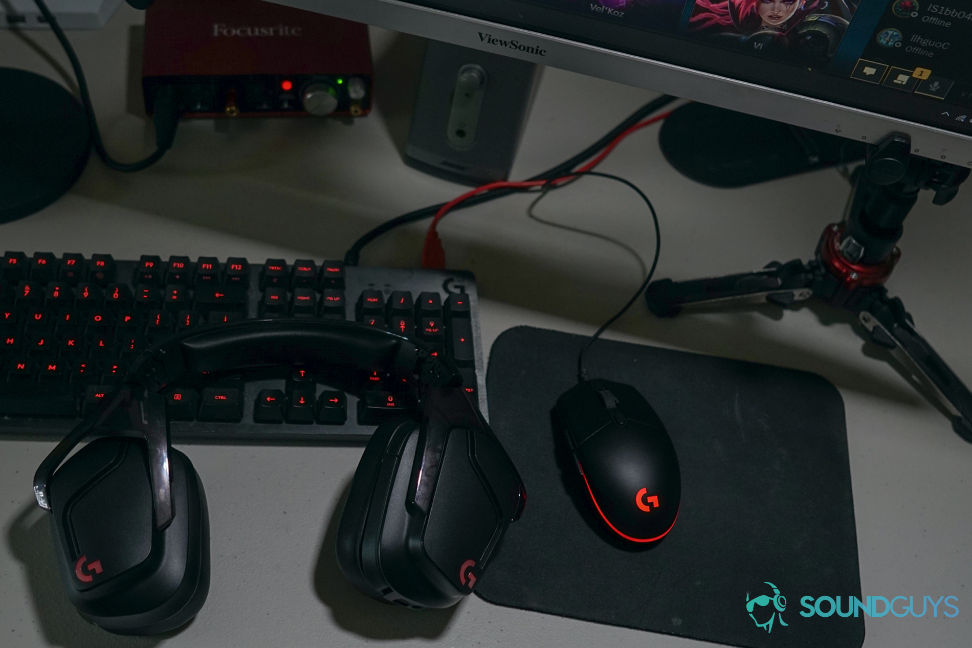 The Logitech G935 gaming headset sits in front of a PC, next to a Logitech gaming mouse and Logitech G413 Carbon mechanical keyboard, with a Viewsonic monitor and Focusrite Scarlet 2i2 audio interface in the background.