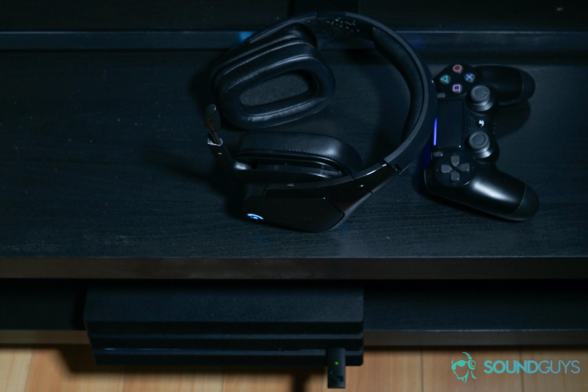 The Logitech G935 gaming headset sits on a black TV stand next to a Playstation 4 DualShock controller, above a Playstation 4
