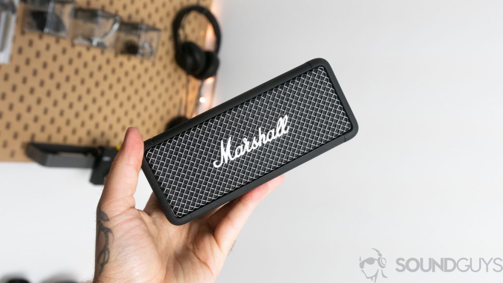 Man holding the Marshall Emberton Bluetooth speaker in hand in front of storage wall
