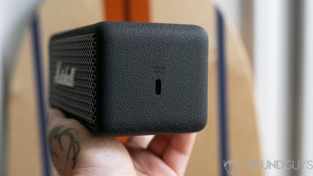 Man holding the Marshall Emberton Bluetooth speaker in front of a balance board with the USB-C input in the center of the shot