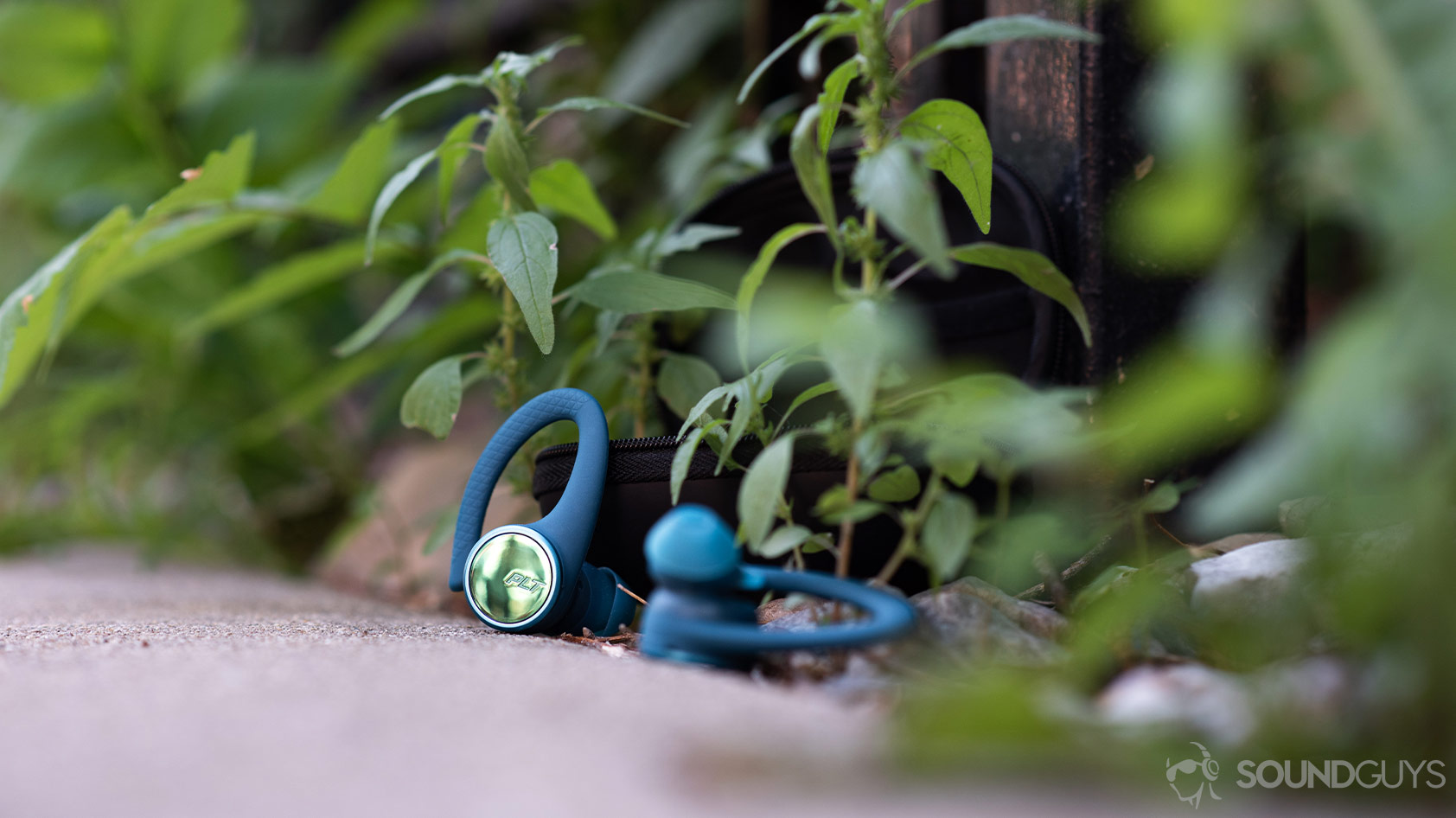 A picture of the Plantronics BackBeat FIT 3200-true wireless workout earbuds outside in front of green foliage peeking through a fence.