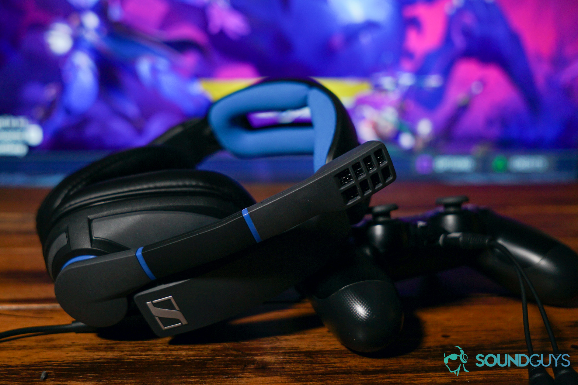 The Sennheiser GSP 300 gaming headset leans on the PlayStation 4 controller it is plugged into, with a Dauntless on Playstation 4 running on a TV in the background.