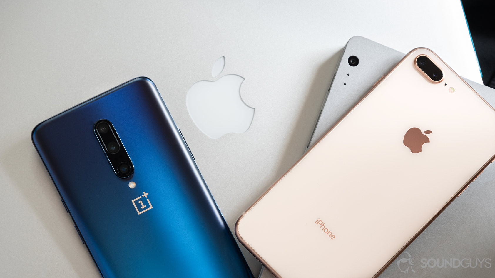 A OnePlus 7 Pro, iPhone 7 Plus, Macbook Pro, and Surface Book Pro all stacked on top of each other to demonstrate how to use Bluetooth across a range of devices.