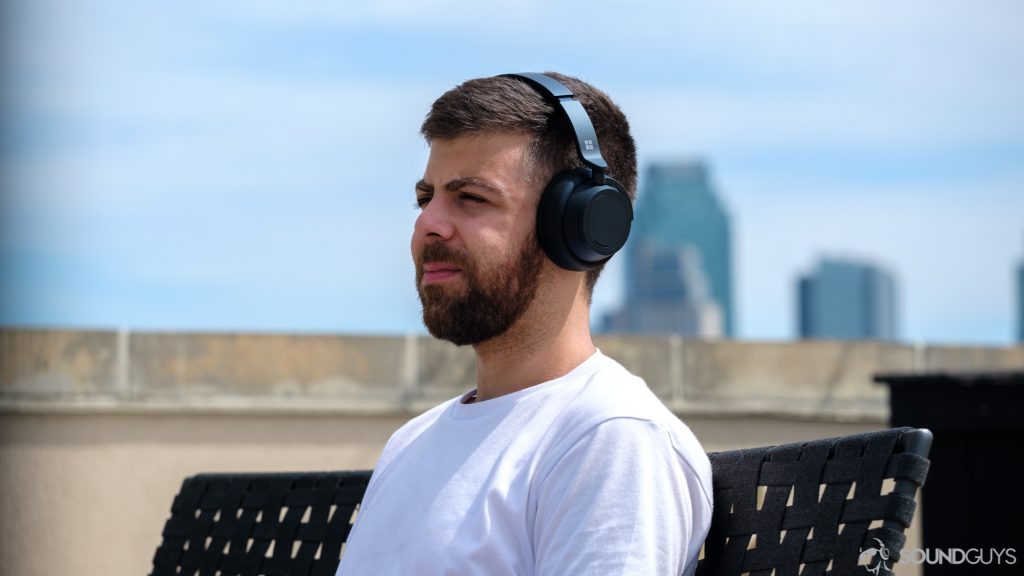 Man in white shirt wearing the Microsoft Surface Headphones 2 on a bench