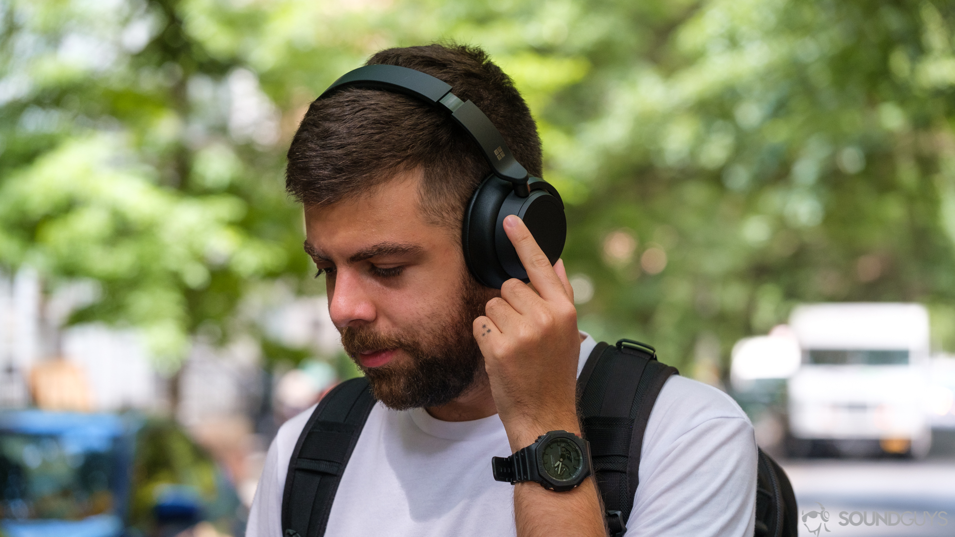 A man rotates the noise canceling ring on the Microsoft Surface Headphones 2 in front of trees.