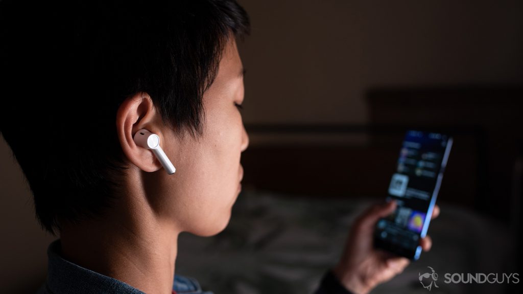 A picture of the OnePlus Buds true wireless earbuds (white) being worn by a woman looking at Spotify on the OnePlus 7 smartphone.