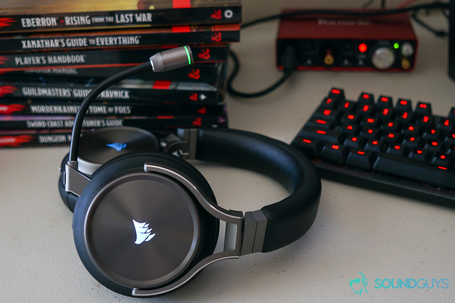 The Corsair Virtuoso Wireless SE sits on a desk next to a Logitech gaming keyboard, a FocusRite Scarlett 2i2, and copies of the Dungeons and Dragons Player's Handbook, Monster Manual, Dungeon Master's Guide, and various associated settings books.