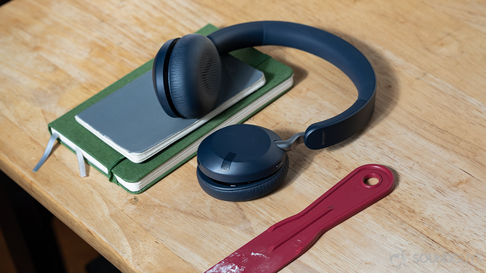 The Jabra Elite 45h on-ear Bluetooth headphones on a wooden surface with journals; the left ear cup is rotated so the interior padding is visible to the viewer.