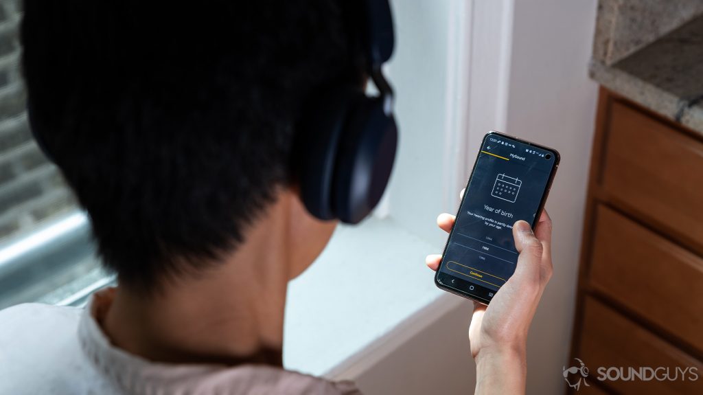 An over-the-shoulder picture of the Jabra Elite 45h on-ear Bluetooth headphones connected to the Jabra MySound+ application on a smartphone held by a woman.