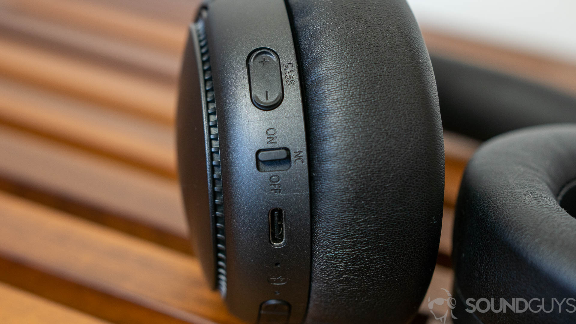Close-up of the bass reactor button on the Panasonic RB-M700B headphones on a wooden bench.