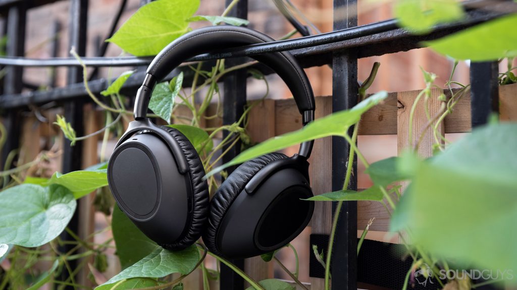 The Sennheiser PXC 550-II noise cancelling headphones hanging in front of a fence and plants.