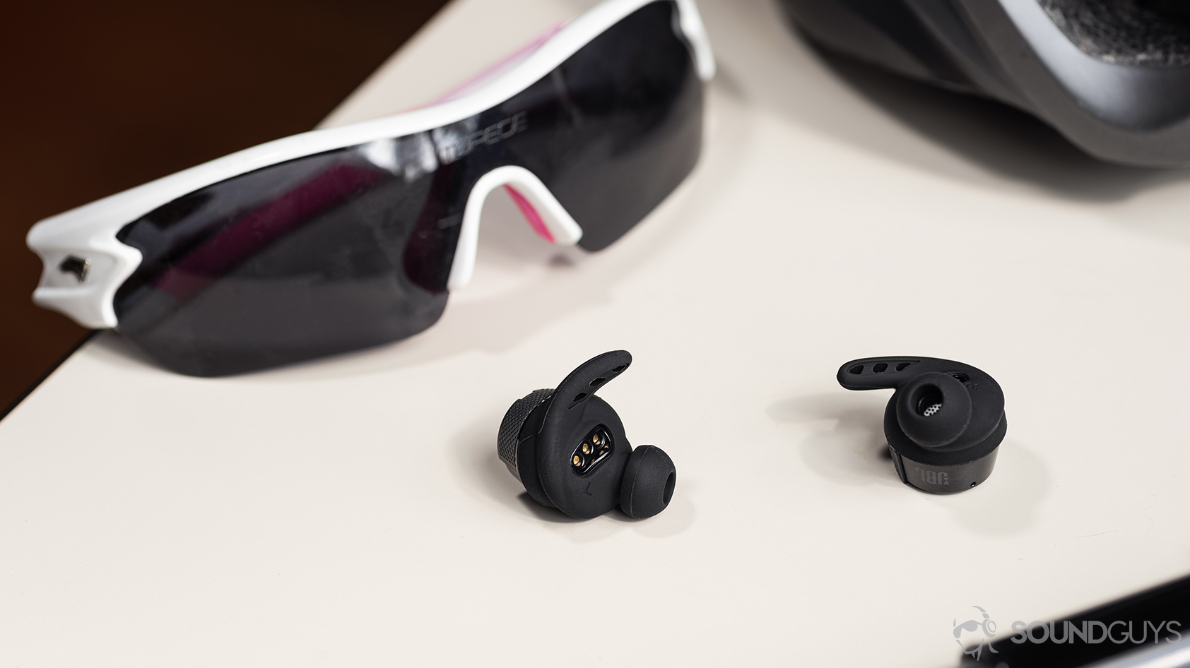 A photo of the UA True Wireless FLASH X by JBL with the wing and ear tips on display in front of cycling glasses on a white table.