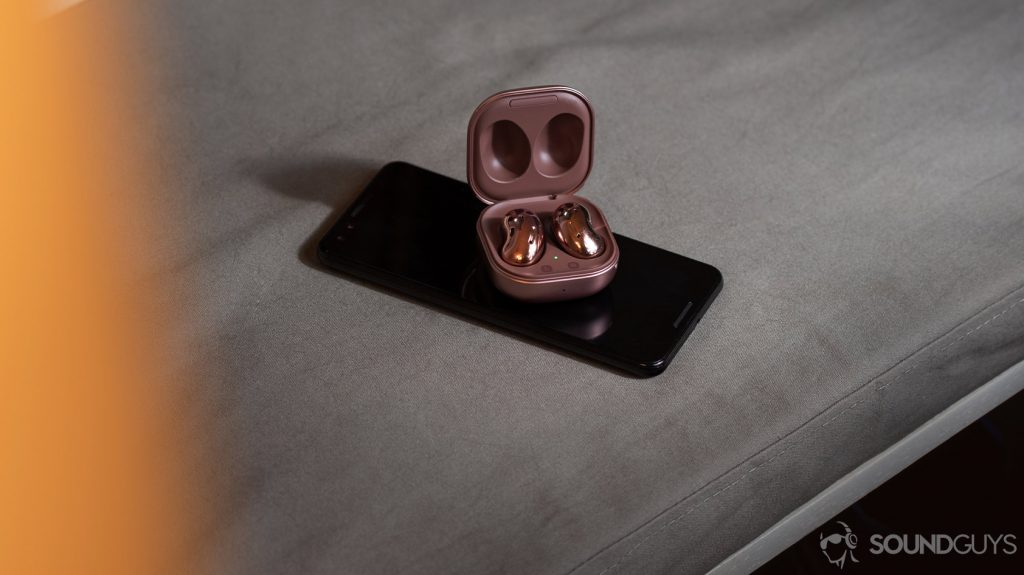 The Samsung Galaxy Buds Live on a Google Pixel 3 smartphone, both of which are on a gray surface.
