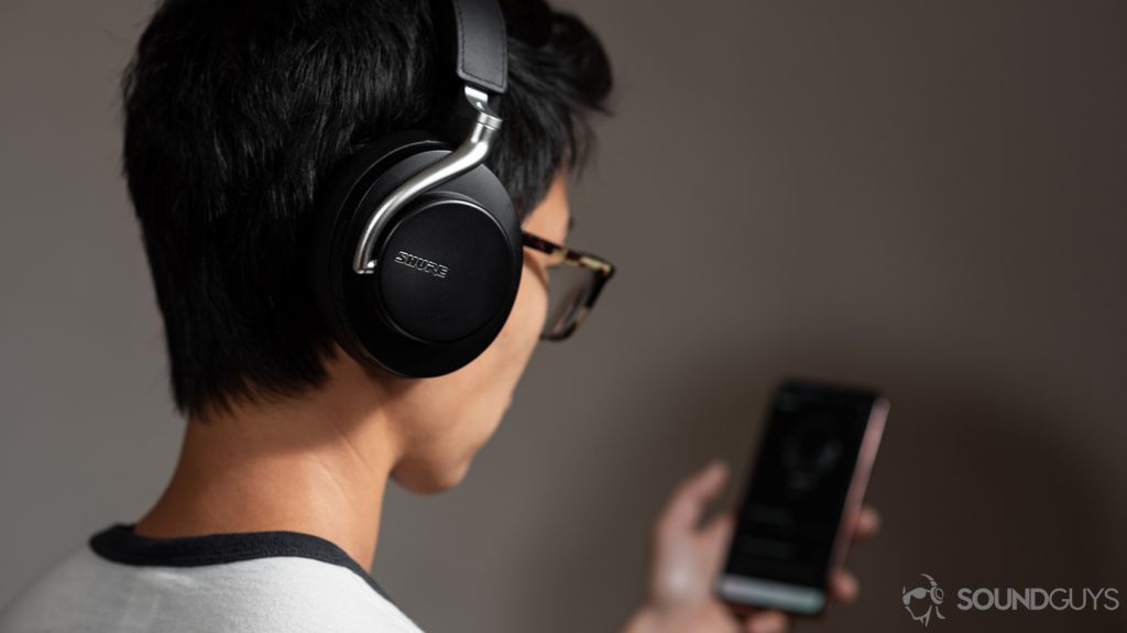 A woman wearing the Shure AONIC 50 noise cancelling headphones and using the Shure PlayPlus headphone app.