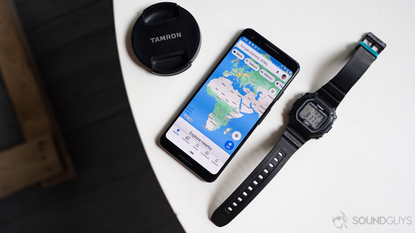 The Google Maps app open on a Google Pixel 3 smartphone, which is flanked by a Tamron lens cap and Casio watch on a white table.
