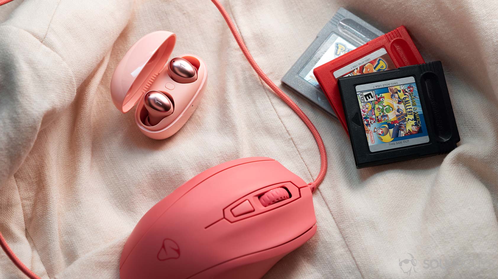 The 1MORE ColorBuds true wireless earbuds next to a pink wired mouse and set of three GameBoy game cartridges.