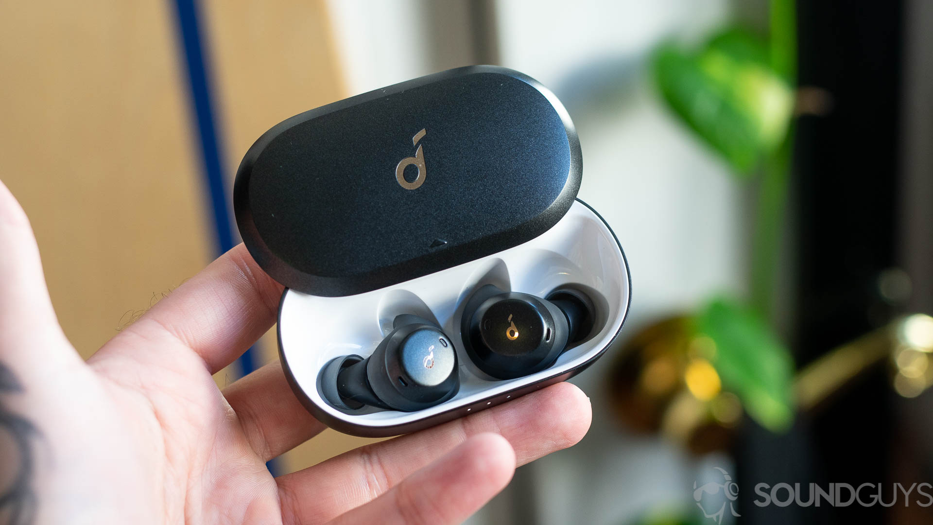 Man holding Anker Soundcore Spirit Dot 2 in hand with lid open and earbuds visible