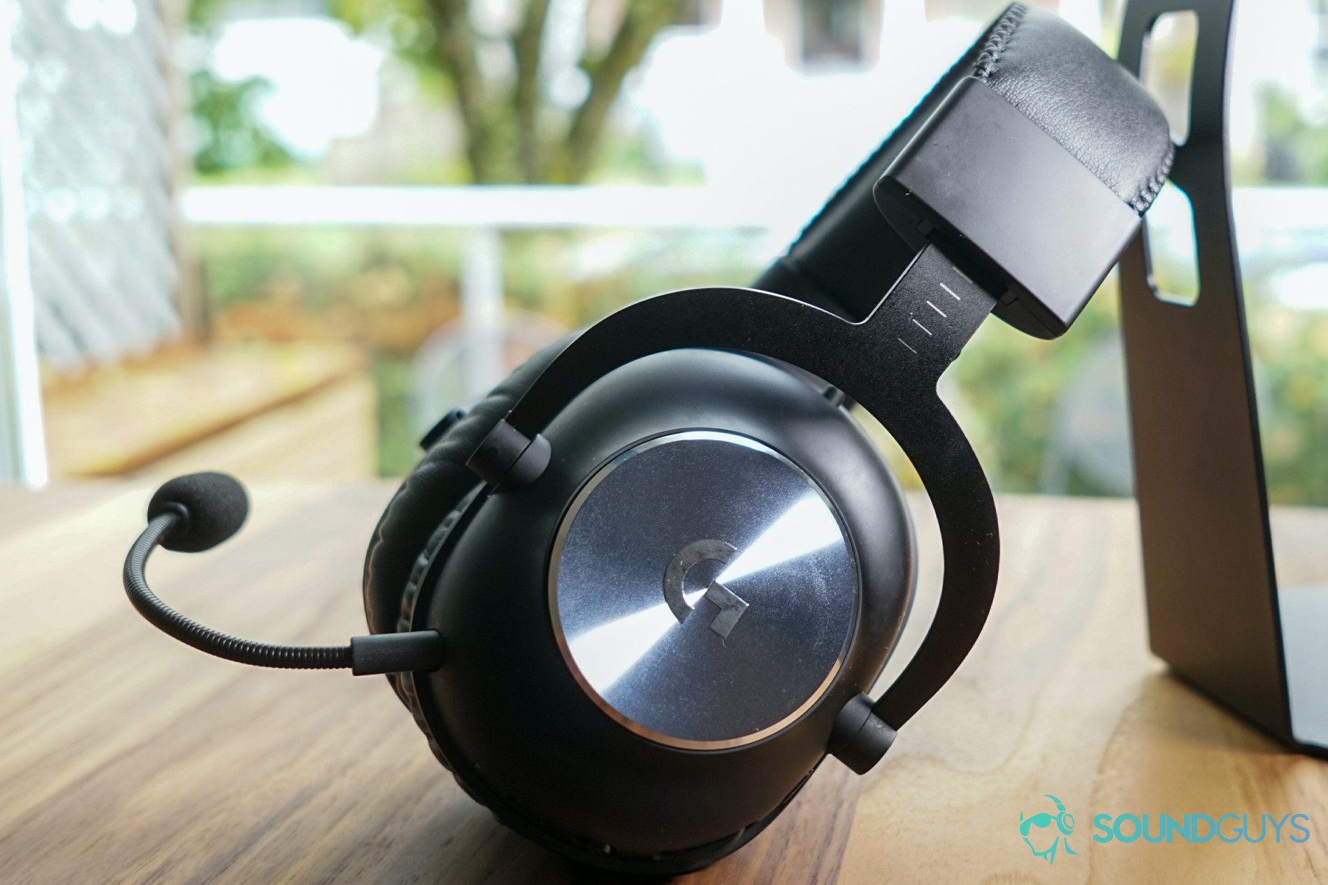 A picture of the Logitech G Pro X Wireless on a wooden table, leaning on the back of a headphone stand.