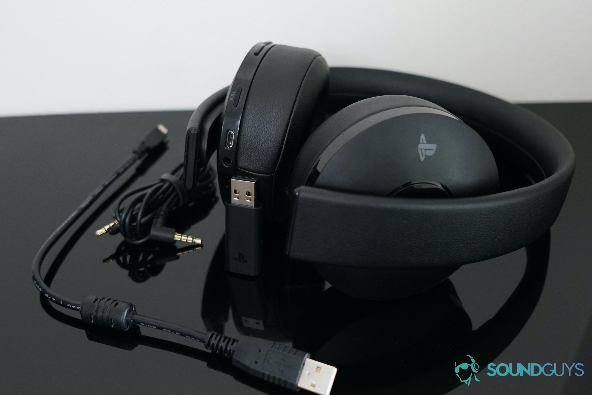 The Playstation Gold Wireless Headset lies on its side with its USB stick and connection cords.