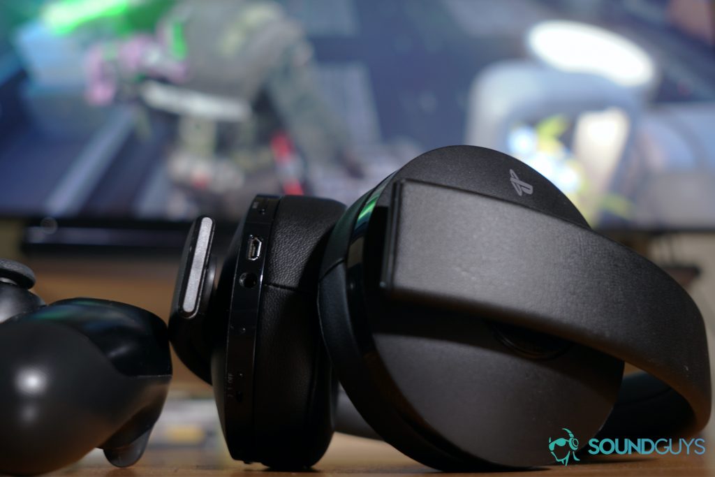 The Playstation Gold Wireless Headset sits on a table next to a Playstation 4 controller in front of a television with Star Wars Jedi: Fallen Order on it.