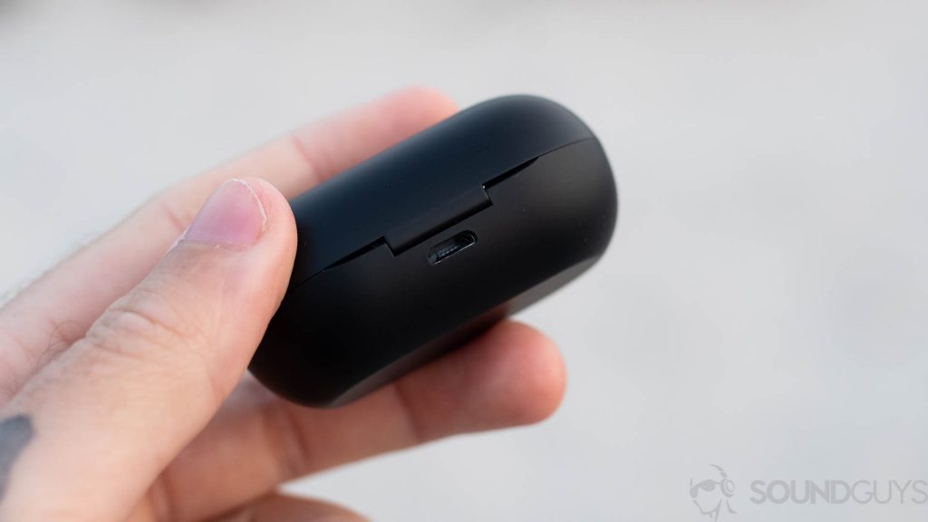 Pictured is a man holding the microUSB charging input of the Raycon E25 earbuds charging case with MicroUSB in focus.