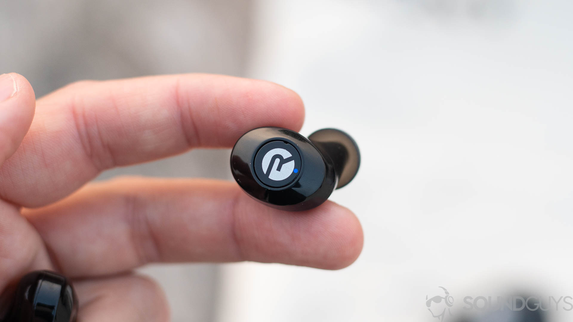 Man holding a single Raycon E25 earbud in fingers with focus on the button