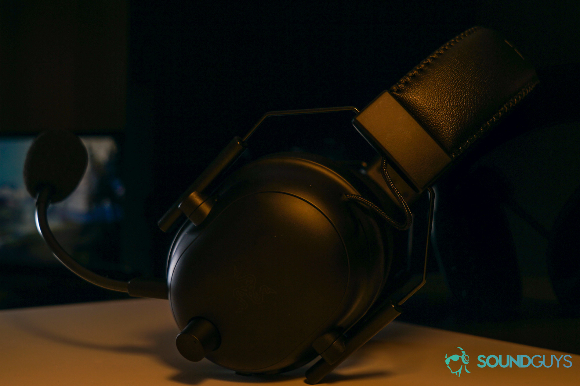 Razer BlackShark V2 Pro shelf shot yellow The Razer BlackShark V2 Pro gaming headset sits on a white shelf in front of a reflective black surface with a monitor displaying a Windows 10 desktop in the reflection.
