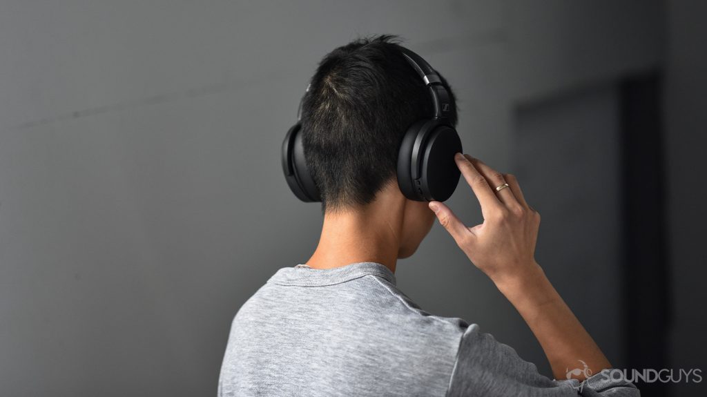 A picture of the Sennheiser HD 450BT noise canceling headphones worn by a woman as she adjusts the volume via the onboard controls on the right ear cup.