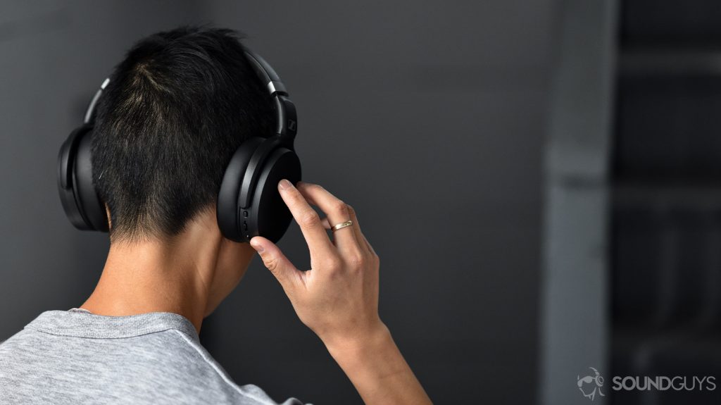 A picture of the Sennheiser HD 450BT noise cancelling headphones worn by a woman as she adjusts the volume via the onboard controls on the right ear cup.