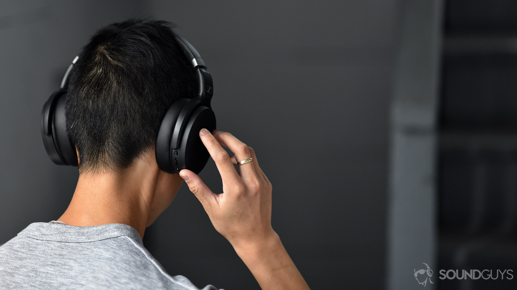 A picture of the Sennheiser HD 450BT noise canceling headphones worn by a woman as she adjusts the volume via the onboard controls on the right ear cup.