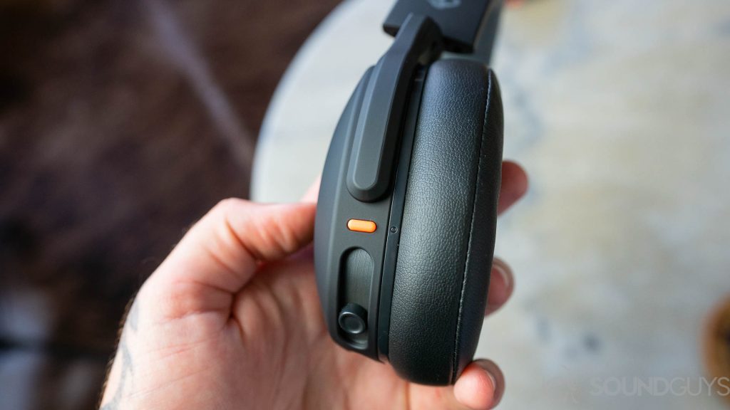 Man holding Skullcandy Crusher Evo in hand with focus on the orange power button.