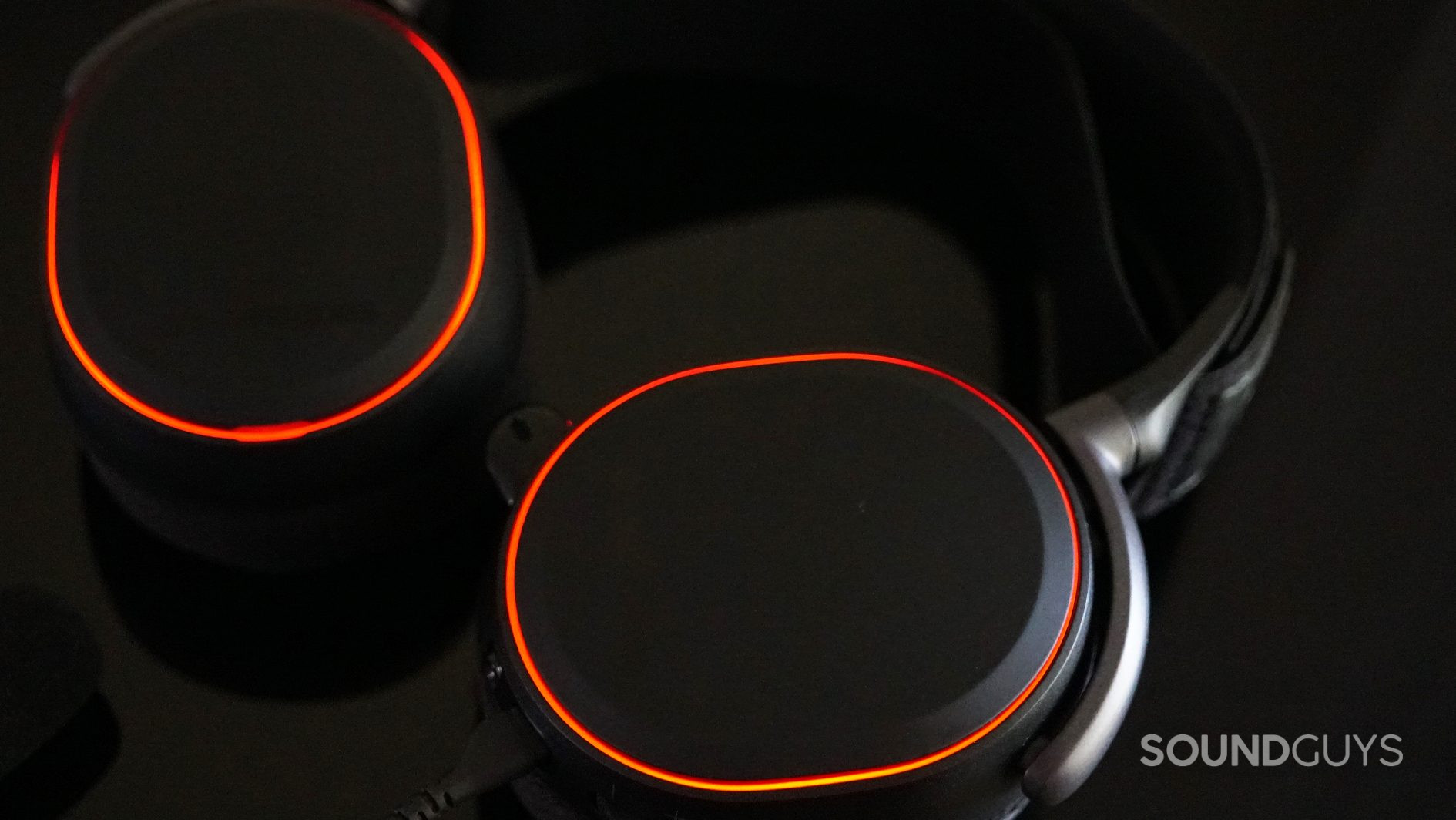 The Arctis Pro lays flat on a black reflective surface with its LED lights glowing orange.