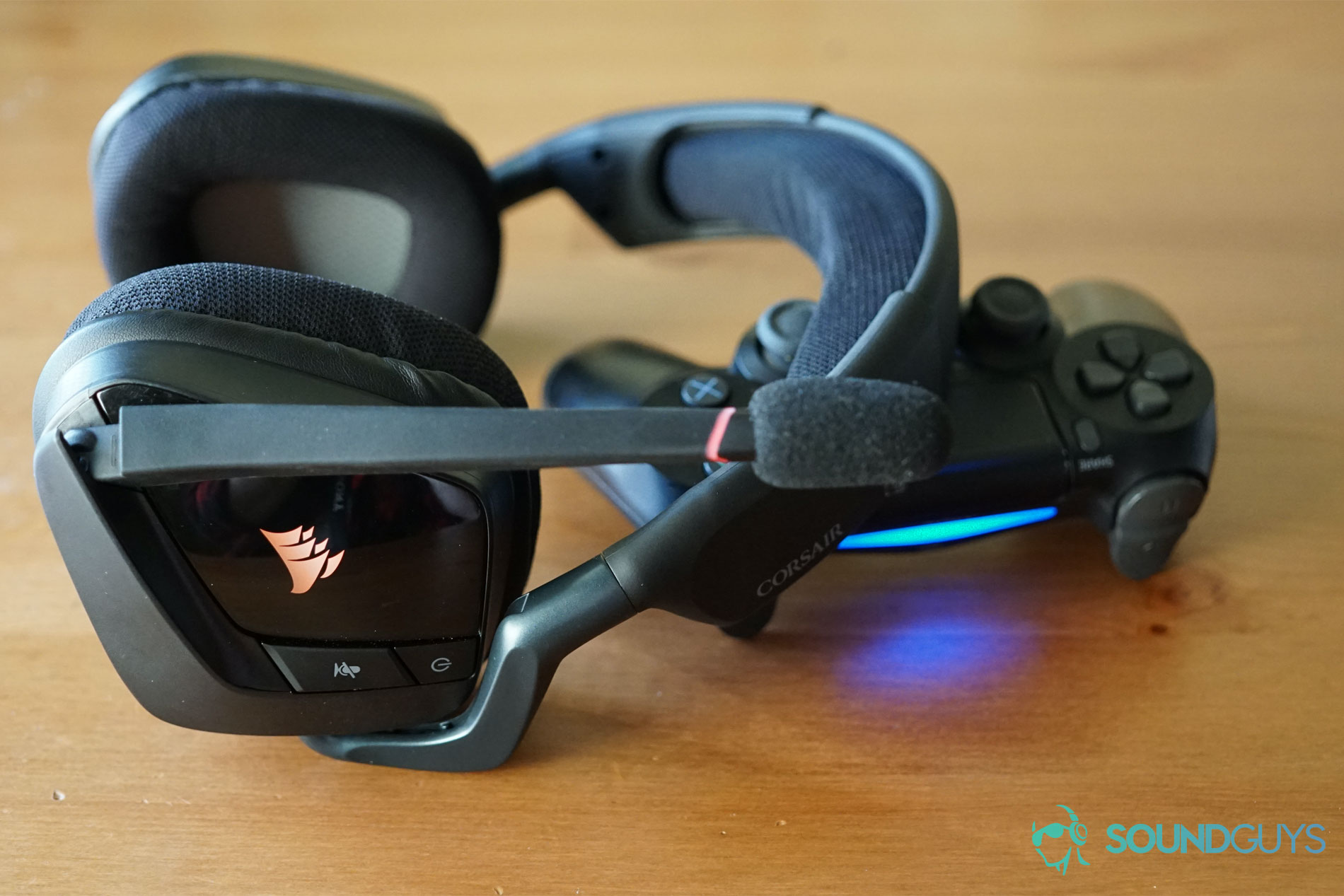 Corsair-Void-RGB-Elite-Wireless gaming headset Playstation 4 controller The Corsair Void RGB Elite Wireless Gaming headset lies on top of a PlayStation 4 DualShock controller on a wooden surface.