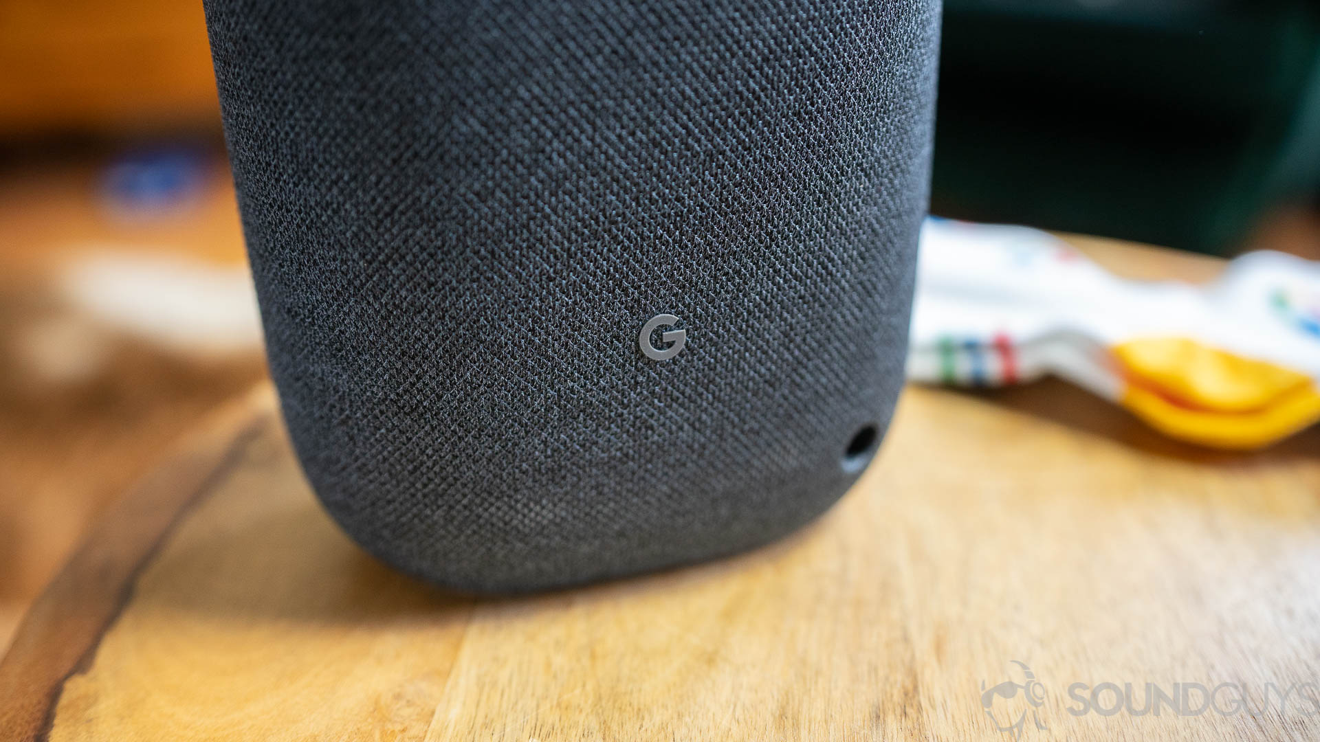 Pictured is the "G" logo on the back on the Google Nest Audio on a wooden surface