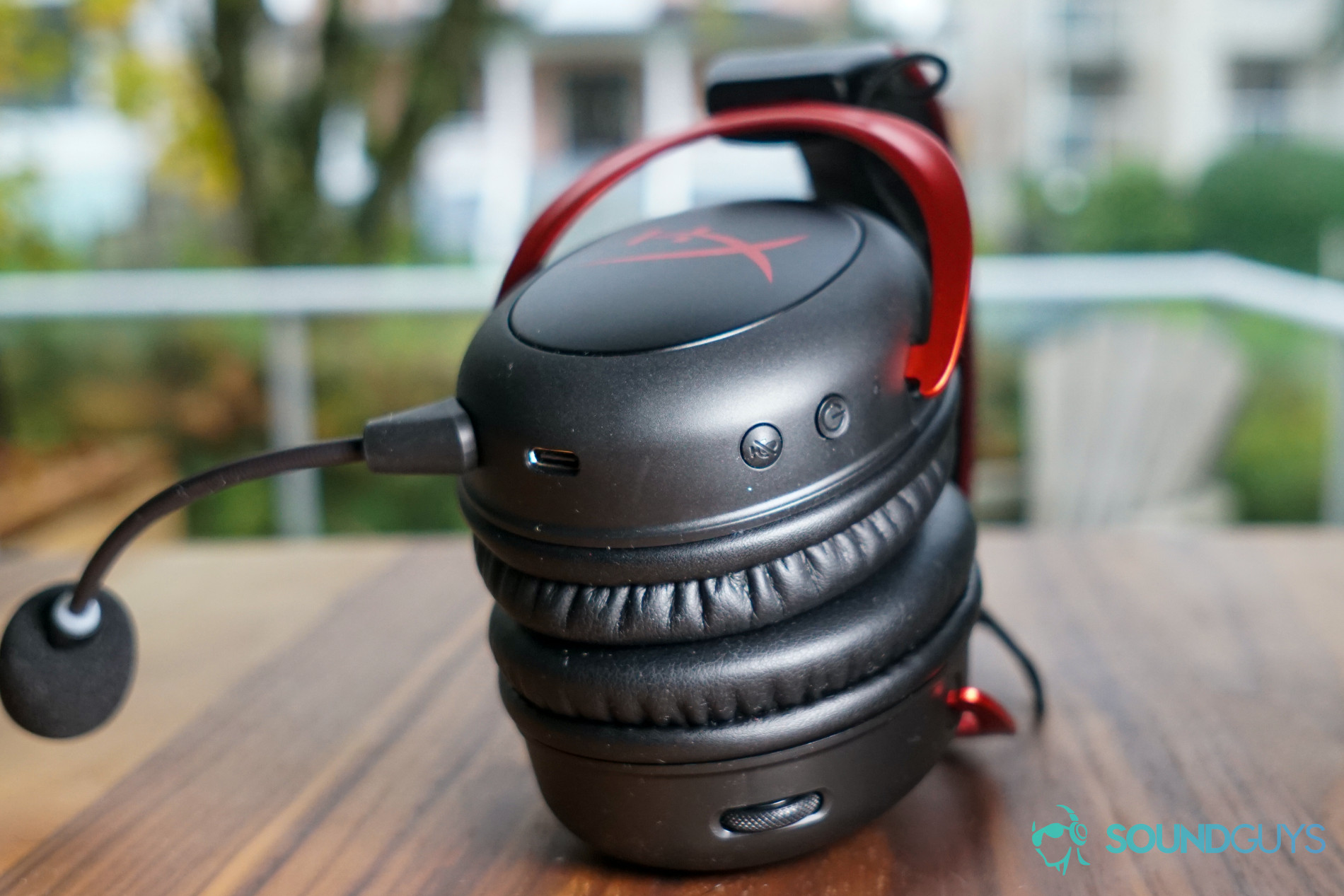 The HyperX Cloud II Wireless gaming headset lays on its side by a window, showing its buttons and charging port.