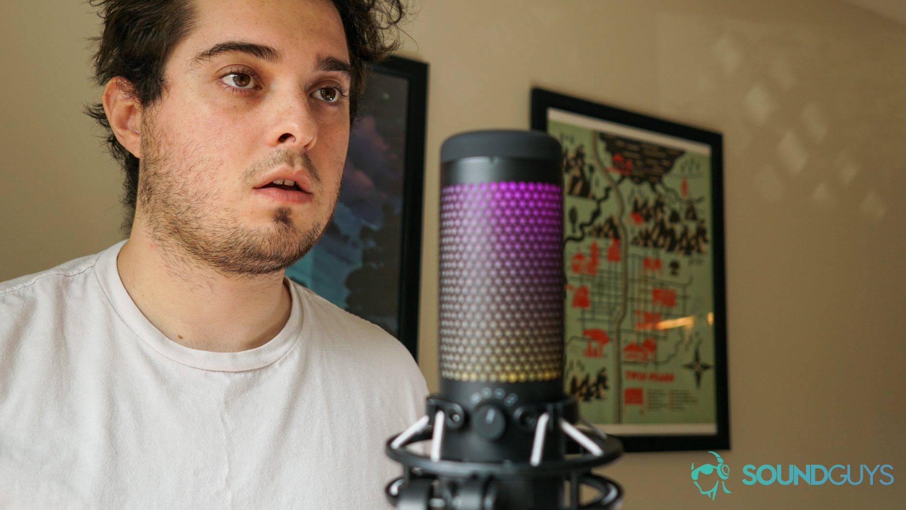 Man positioned behind the HyperX QuadCast S. Wall hangings are visible in the background.