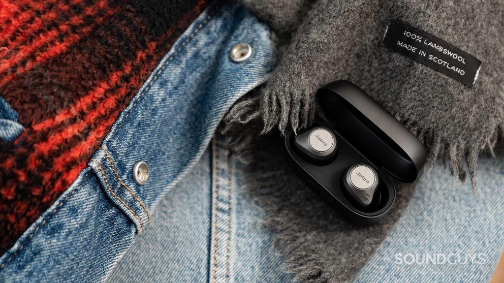 The Jabra Elite 85t noise cancelling true wireless earbuds in an open case and on top of a denim jacket.