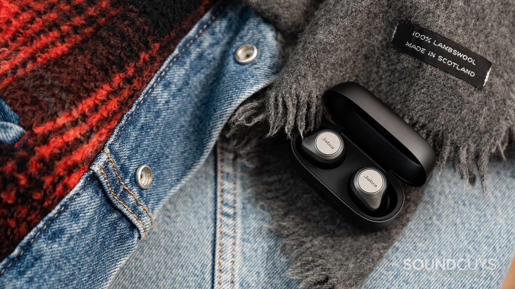 The Jabra Elite 85t noise canceling true wireless earbuds in an open case and on top of a denim jacket.
