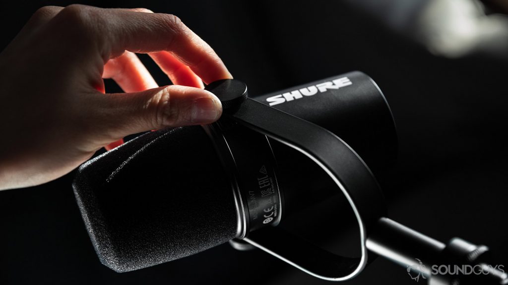 A hand adjusts the Shure MV7 USB microphone's yoke tightness.