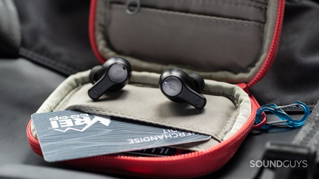 The 1MORE PistonBuds cheap true wireless earbuds on top of an open wallet with a giftcard pulled out for a size reference.
