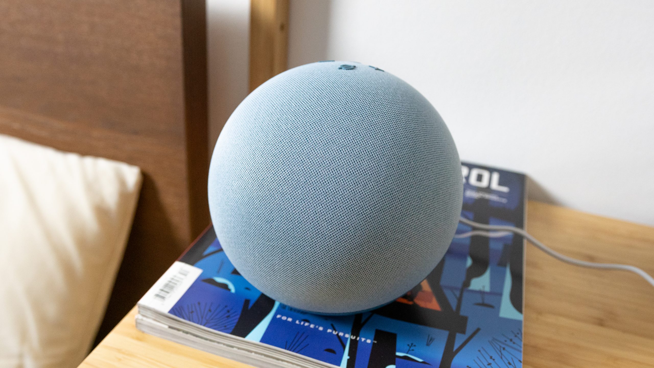 The Amazon Echo 4th gen on a bedside table with bed in the background.