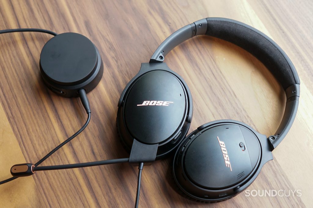 The Bose QuietComfort lays flat on a wooden table plugged into its volume dial.