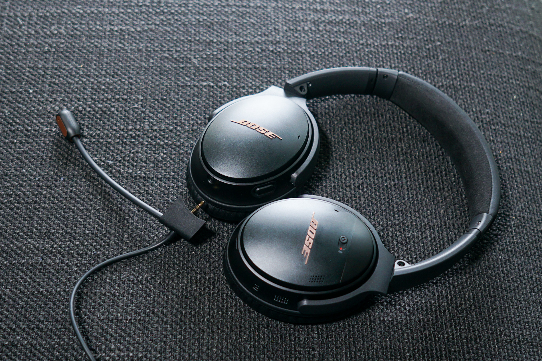 The Bose QuietComfort 35 II Gaming Headset lays on a fabric surface next to its detachable microphone.